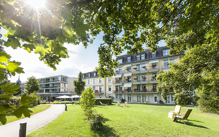 Ein Blick auf das Gebäude der Reha Rheinfelden, ausserhalb im Park. Die Sonne scheint.